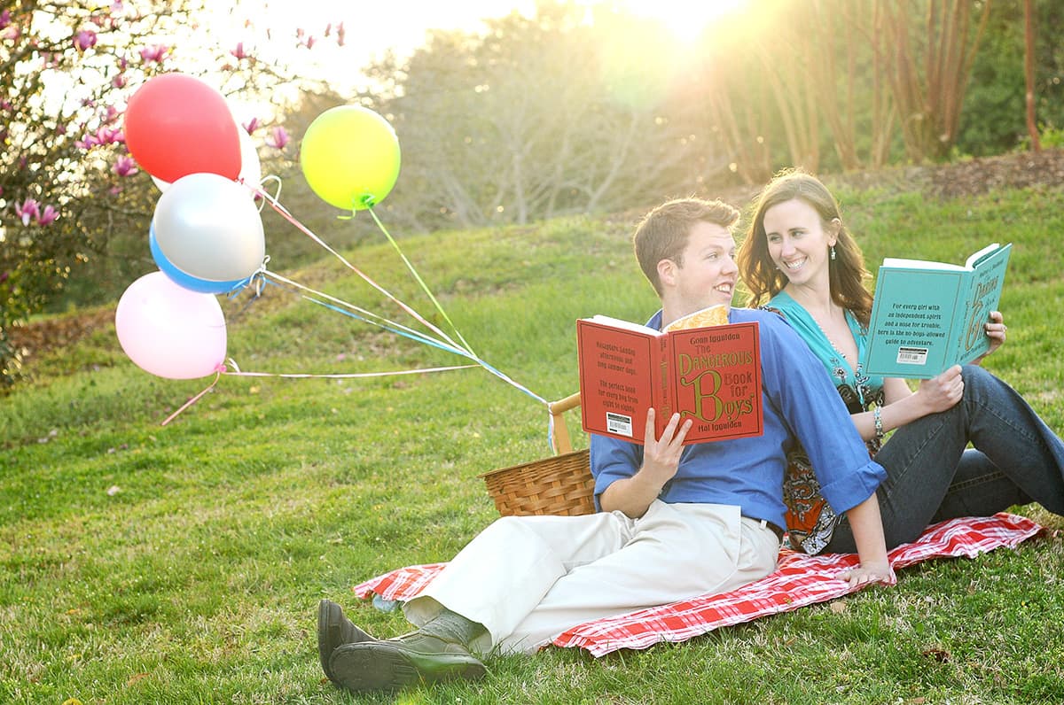 Reading Dangerous Book for Boys and the Daring Book for Girls at engagement pictures with a picnic basket and balloons in Clemson, SC